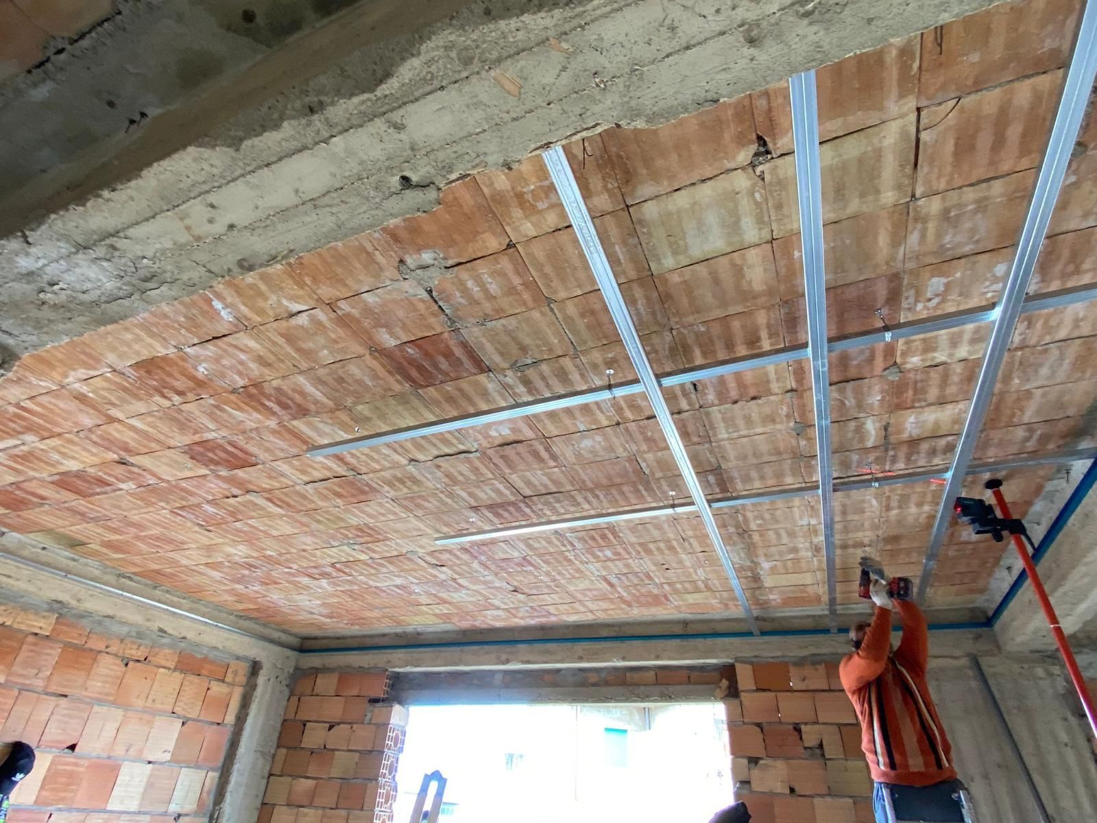 Operaio edile che installa la struttura metallica del soffitto in una stanza in mattoni grezzi.