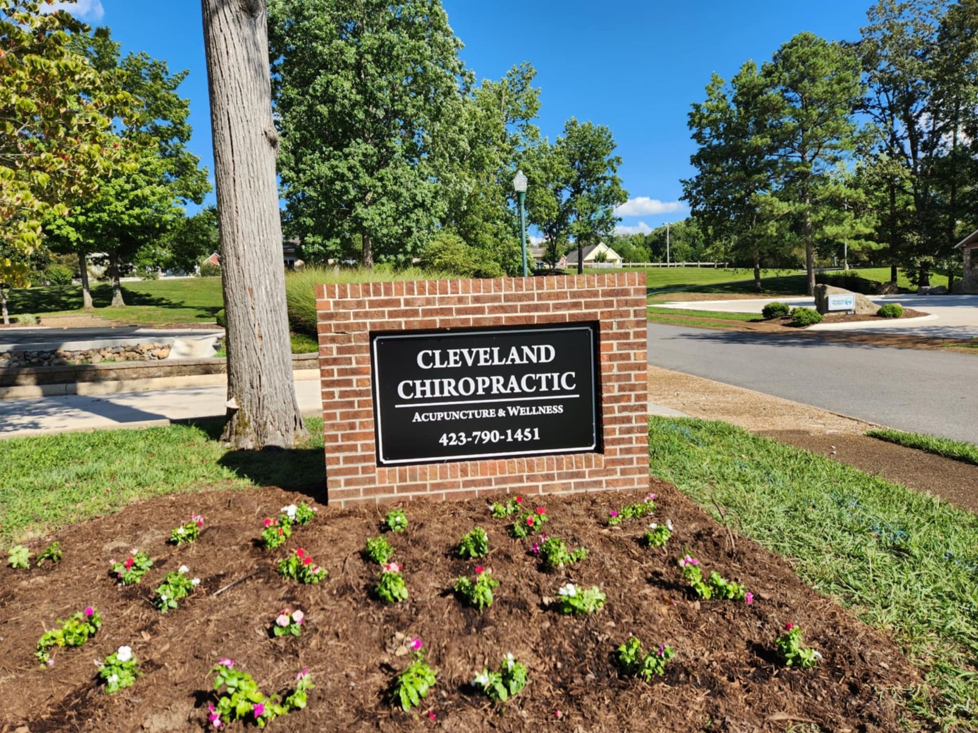 Sign for Cleveland Chiropractic, brick base, text on black background, surrounded by flowers, park setting.
