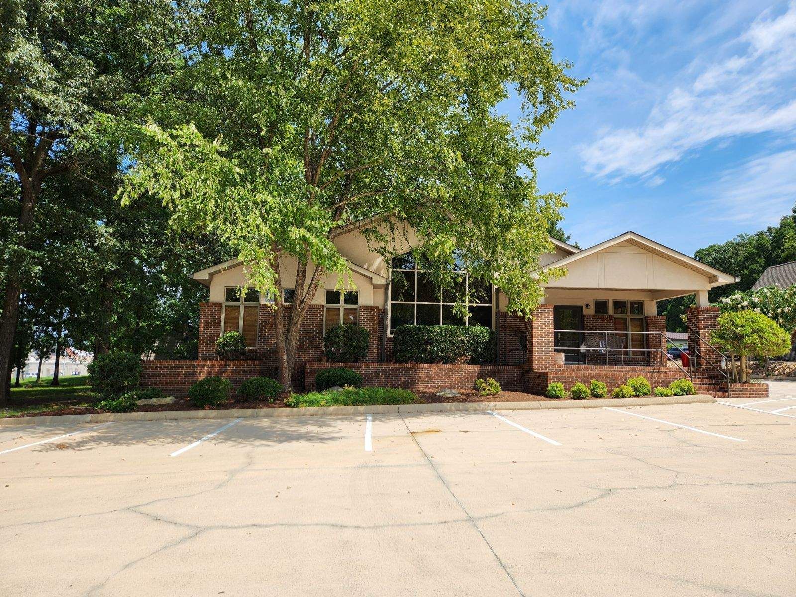 A one-story building with a brick facade and large windows, surrounded by trees and a parking lot.