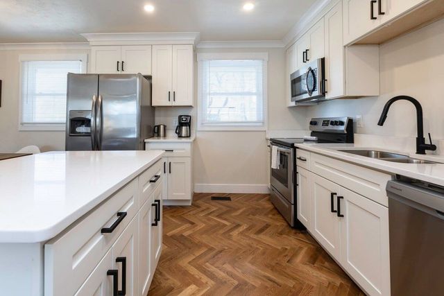 White kitchen with stainless steel appliances, white cabinets, and herringbone wood floor.