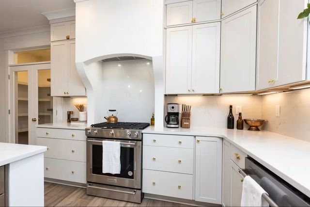 White kitchen with stainless steel appliances, white cabinets, and gold hardware.