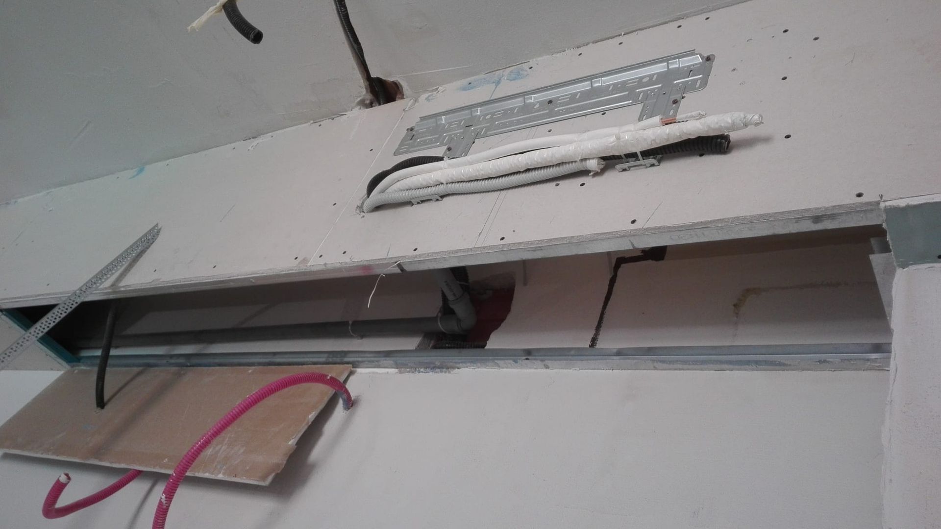 Pannello elettrico a muro aperto con fili a vista e un cavo rosa penzolante