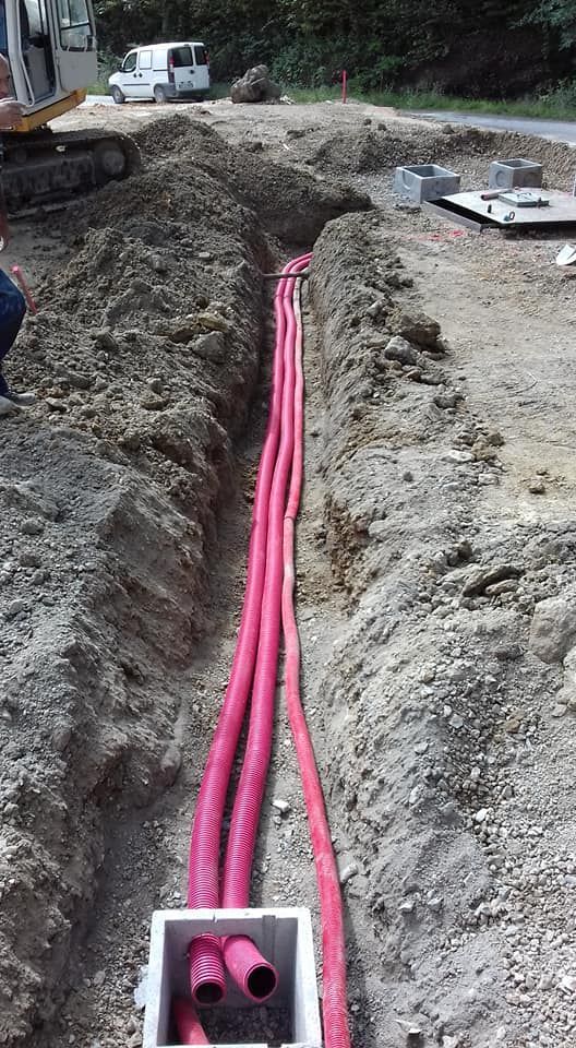 Tubature di servizio rosa in una trincea in un cantiere, con un escavatore nelle vicinanze.