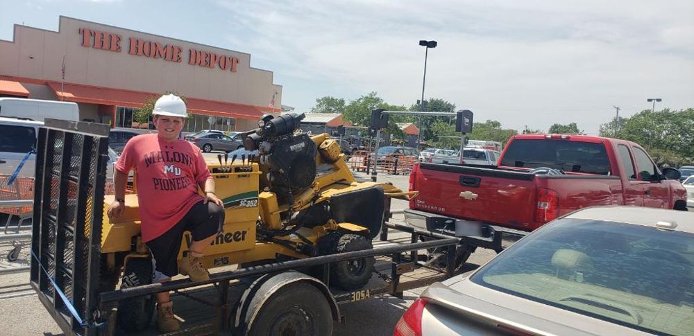 A man is sitting on a trailer with a lawn mower on it.