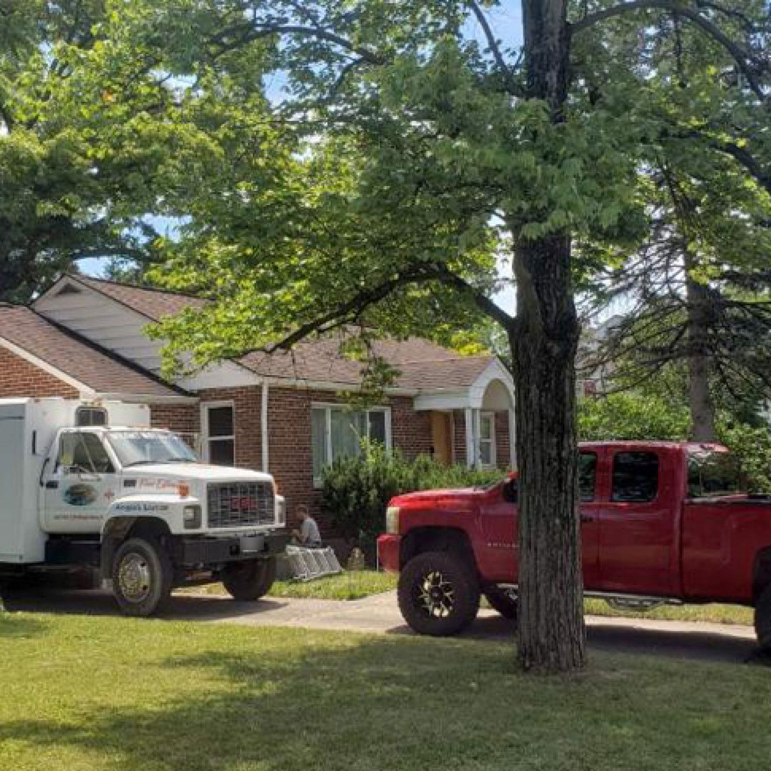 A red truck and a white truck are parked in front of a house.