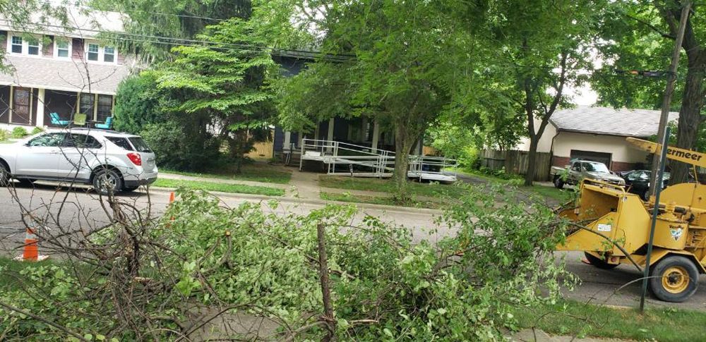 A yellow tree chipper is cutting a tree in front of a house.