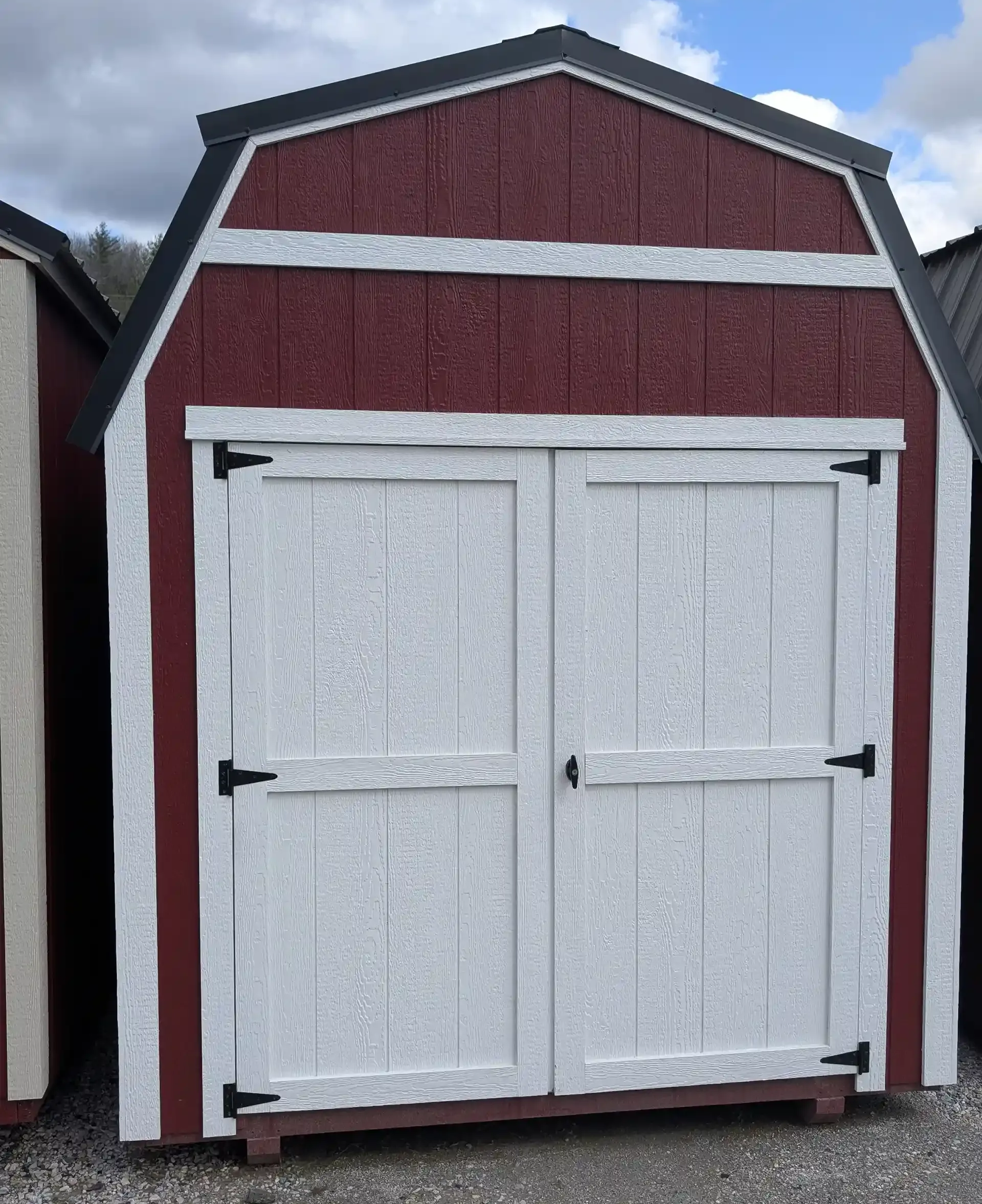 Red and white barn-style shed with double doors, black hardware, and dark roof trim.