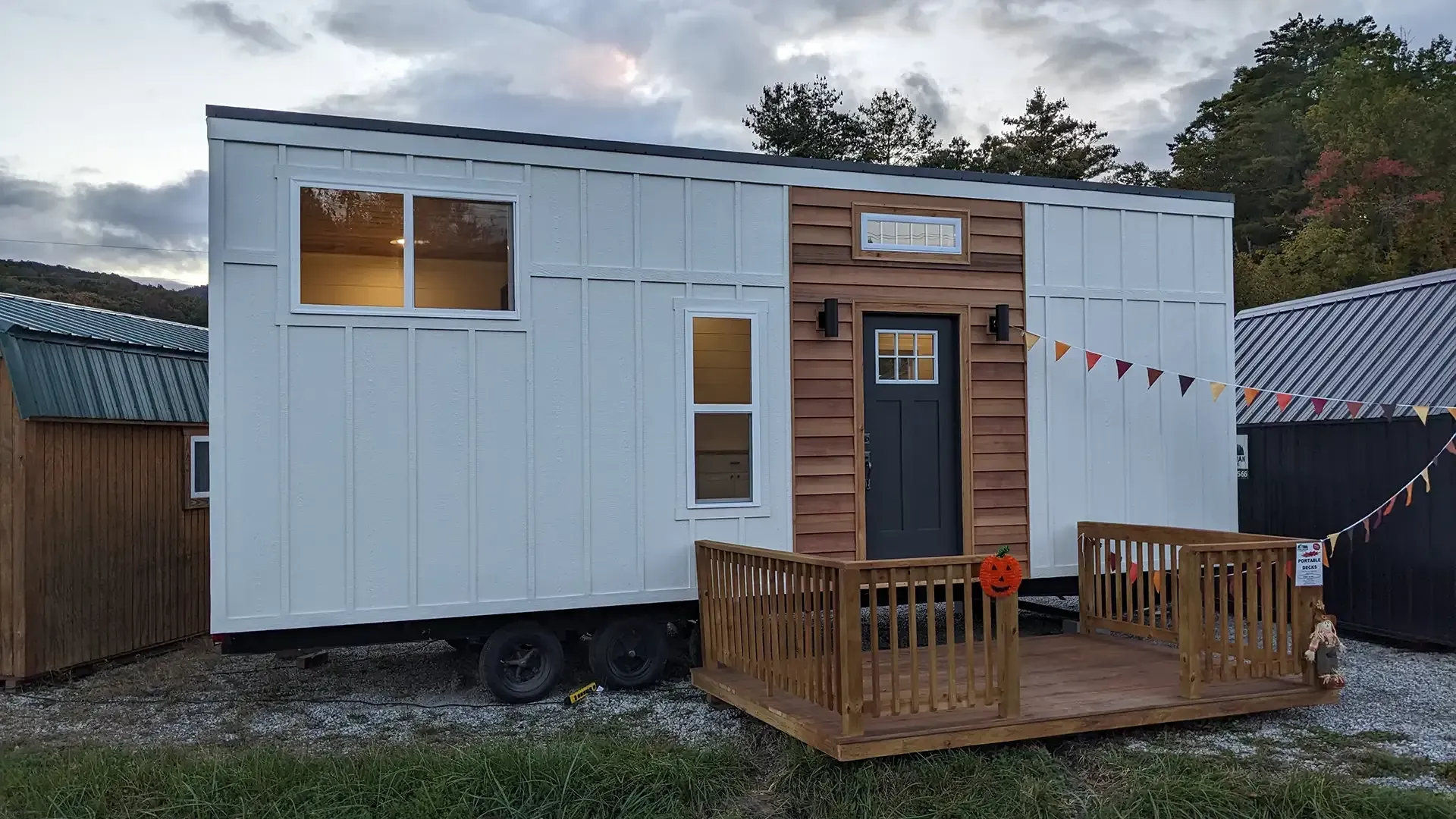 Tiny white house with a wooden porch and dark door, set on a trailer in a grassy area.