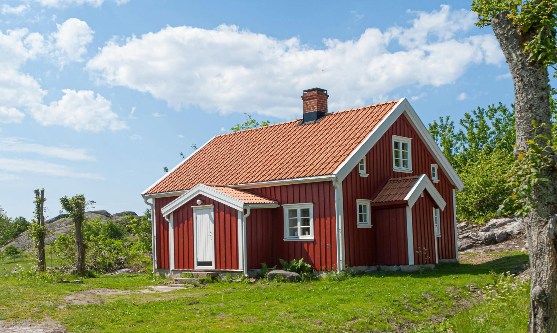 Red wooden house with orange roof, white trim, and small front porch against a blue sky.