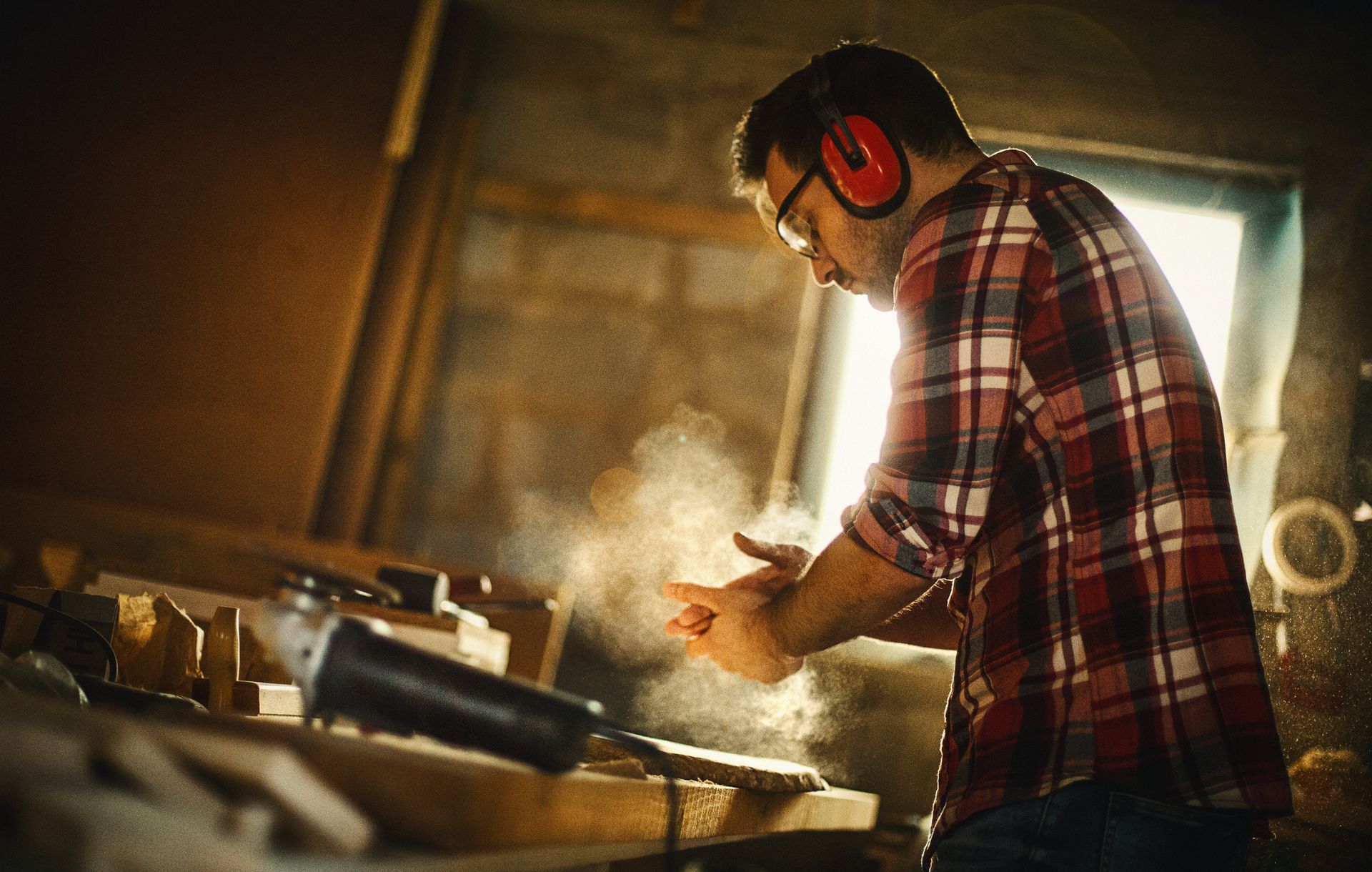 A man wearing ear muffs is working on a piece of wood in a workshop.