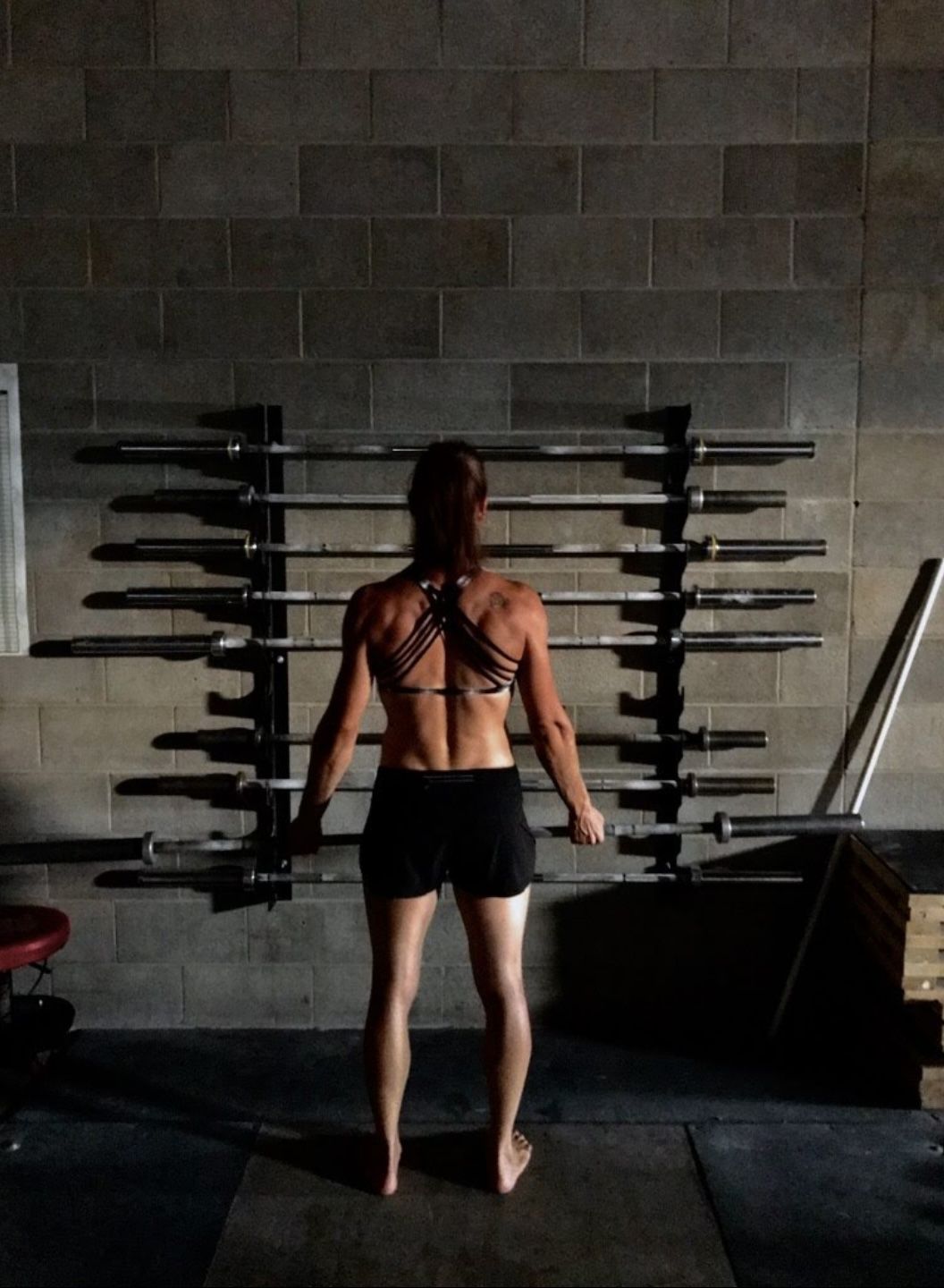 A muscular person in a grey tank top and shorts performs a single-arm kettlebell deadlift in a gym.