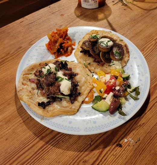 Two flatbreads topped with meat, mushrooms, and cream, served with a small side of shredded carrots and Greek salad.