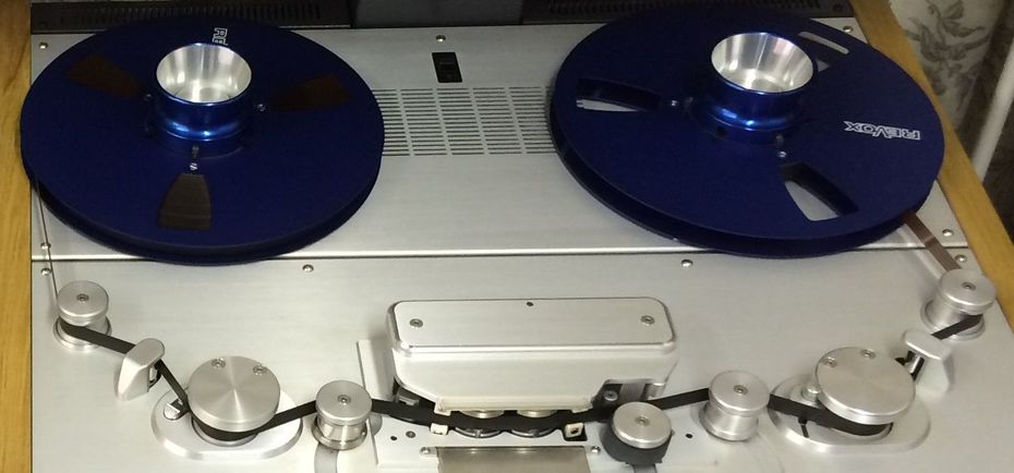 A vintage reel-to-reel tape recorder with two blue reels, metallic components, and a black tape.