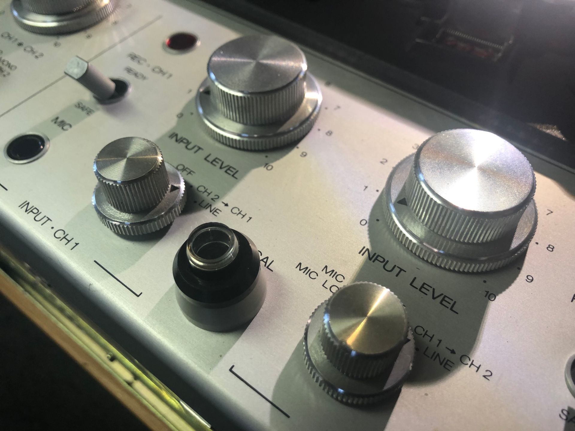 Close-up of a mixing console showing silver knobs and black inputs on a white surface.
