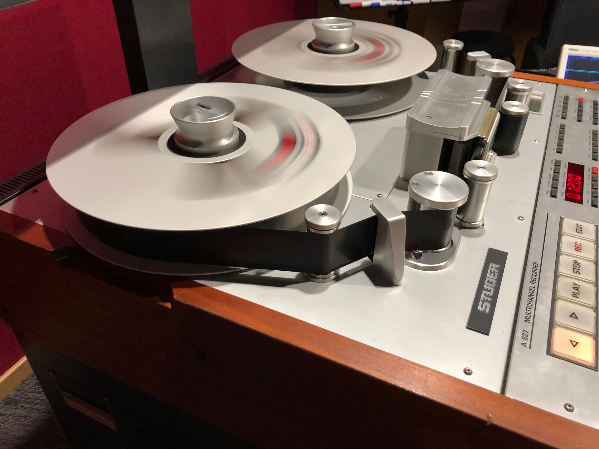 A Studer reel-to-reel tape recorder with spinning reels, in a studio setting.