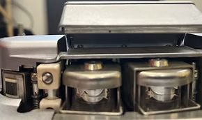 Close-up of a tape deck's internal components, featuring two reel hubs under a metal plate.
