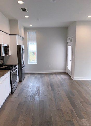 An empty kitchen with hardwood floors , white cabinets , a refrigerator , microwave , and stove.