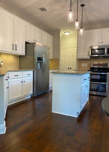A kitchen with white cabinets , stainless steel appliances , hardwood floors and a large island.