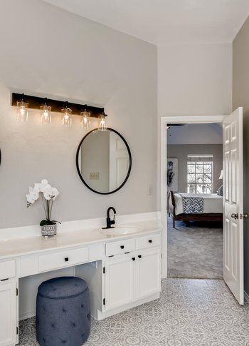 A bathroom with a vanity , sink , mirror and ottoman.