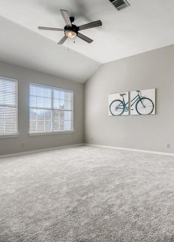 An empty bedroom with a ceiling fan and a bicycle painting on the wall.