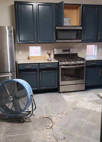 A kitchen with blue cabinets , a stove , a refrigerator , and a fan.
