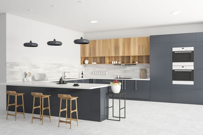 A kitchen with white cabinets , granite counter tops , stools and a trash can.