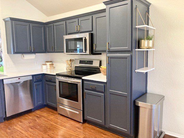 A kitchen with blue cabinets , stainless steel appliances , and a trash can.