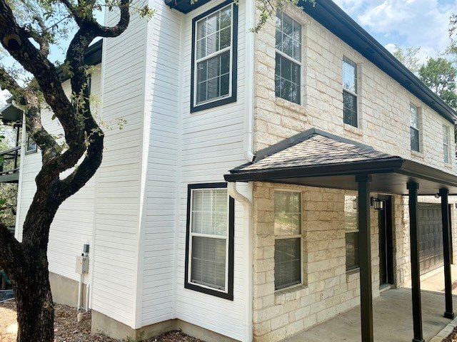 A white house with a porch and a tree in front of it.
