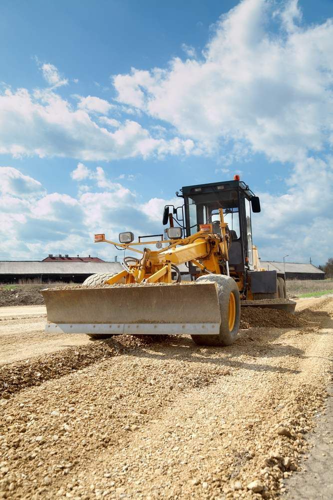 A Yellow Bulldozer is Driving Down a Dirt Road — Pat McDonnell Earthmoving in Bowen, QLD