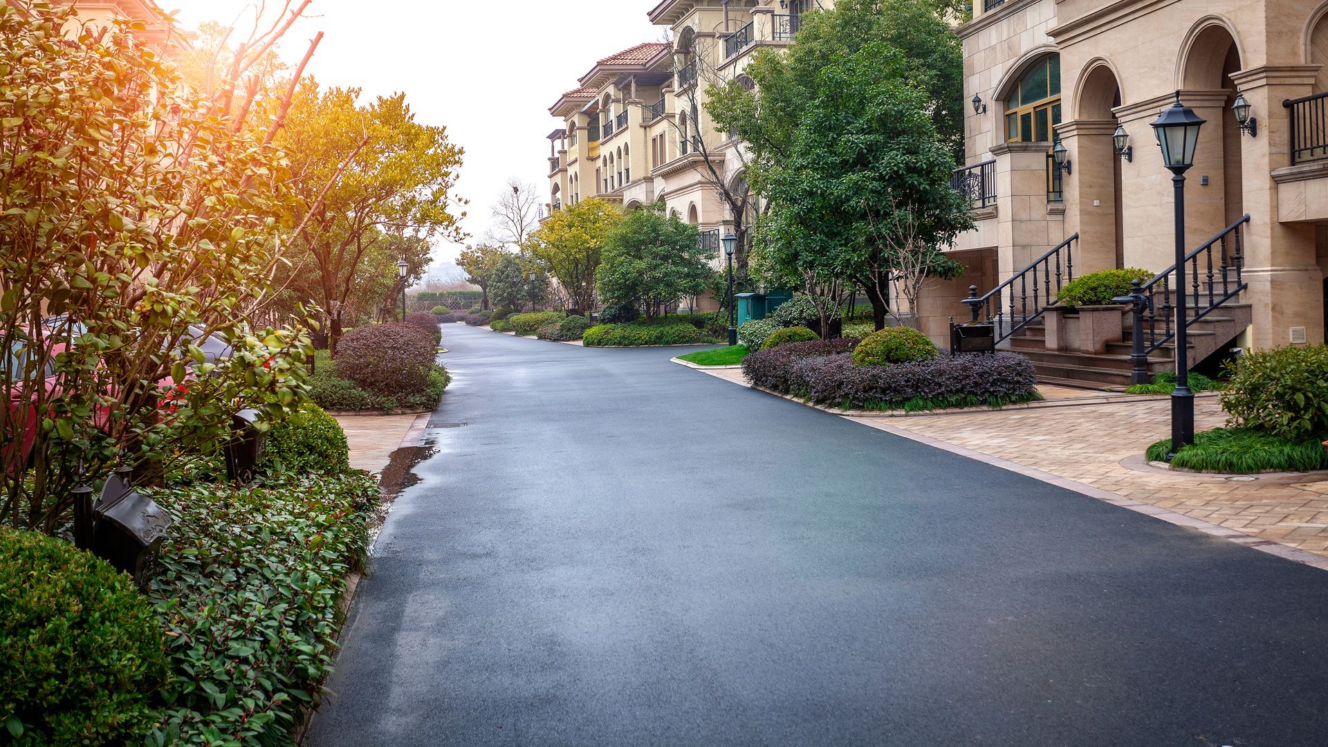 Asphalt road lined with lush landscaping and beige buildings on a cloudy day.