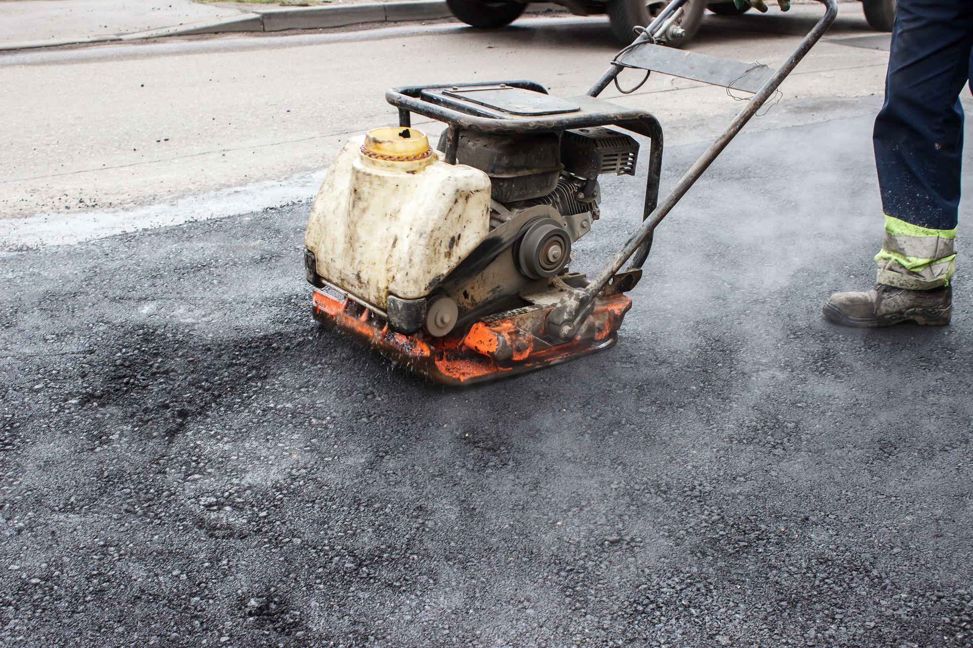Worker using a plate compactor on fresh asphalt, road repair.