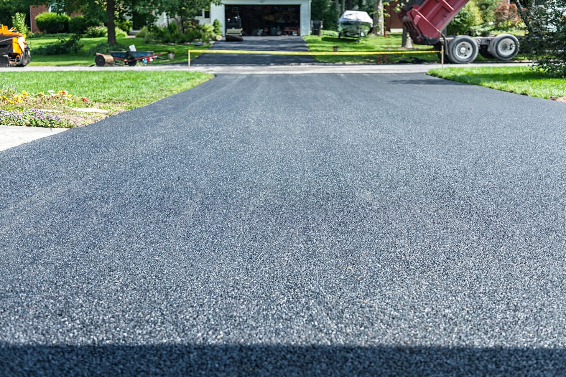 Freshly paved asphalt driveway with truck in background.