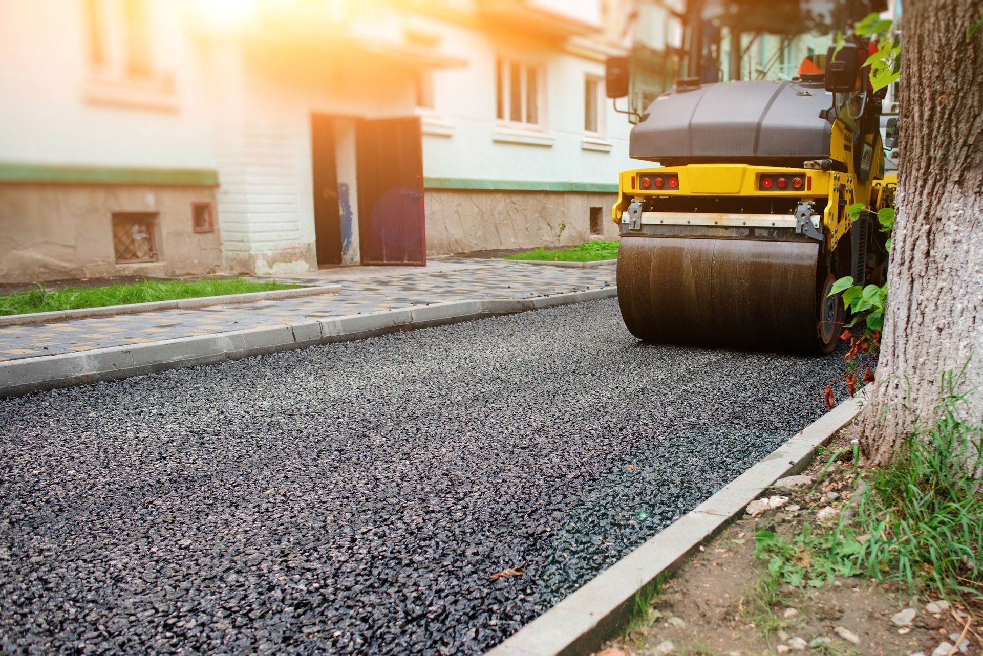 Road roller compacting fresh asphalt on a residential street.