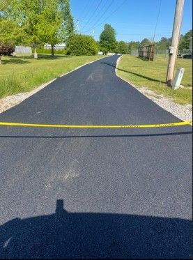 Freshly paved asphalt road with yellow caution tape, surrounded by green grass and trees.