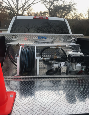 A truck bed with a diamond-plated metal toolbox containing a hose reel, engine, and equipment.