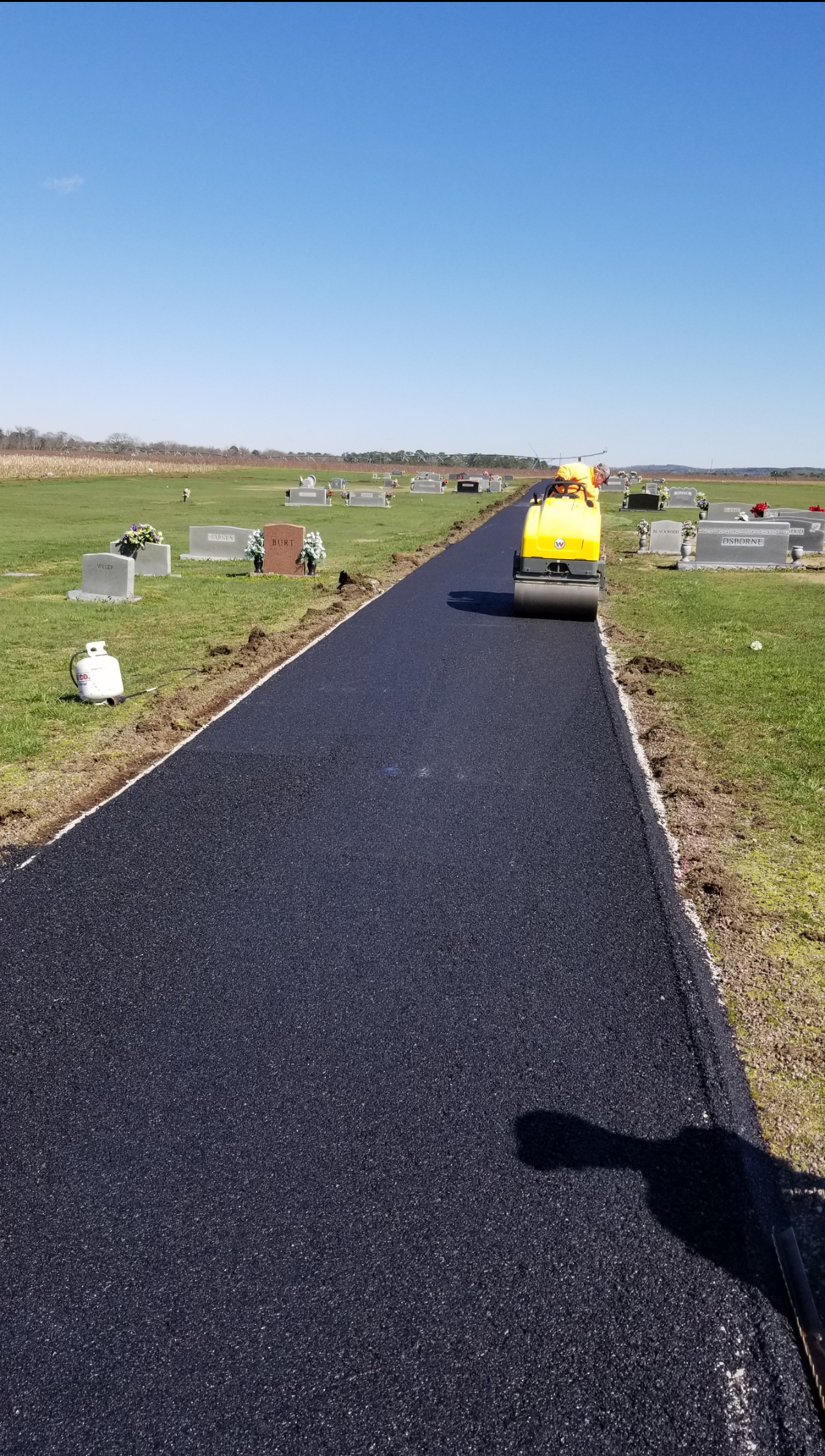 Road roller compacting fresh asphalt on a street; worker raking the edge.