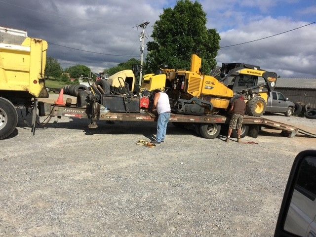 Road worker stands beside a road roller on a sunny street, wearing safety gear.