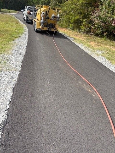 Workers applying sealant to a road crack with a tool, orange cone visible.