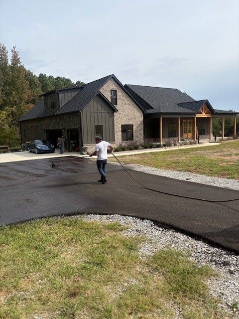 Person applying black sealant to asphalt with a squeegee on a driveway.