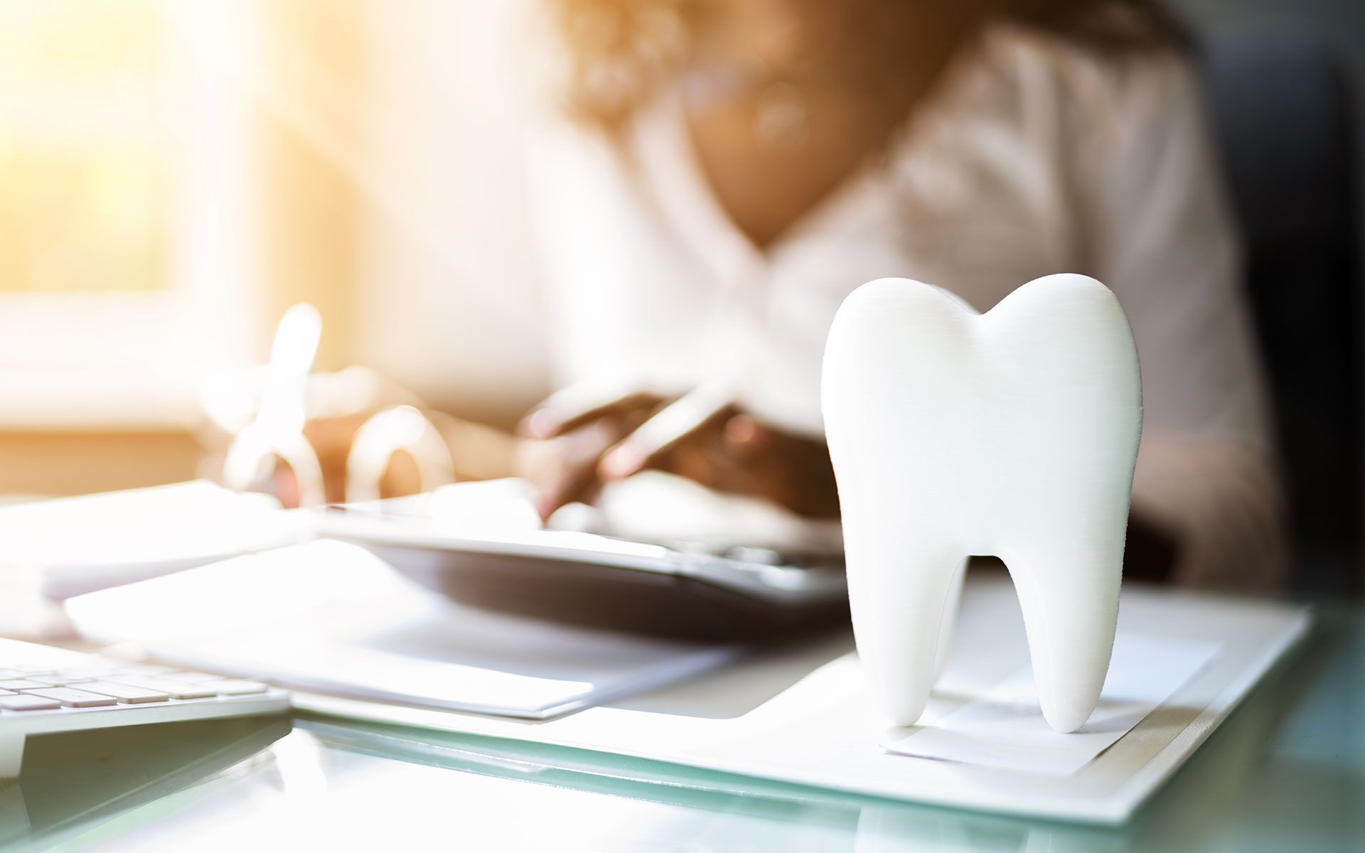 White tooth model on papers, blurred person working at desk with calculator.