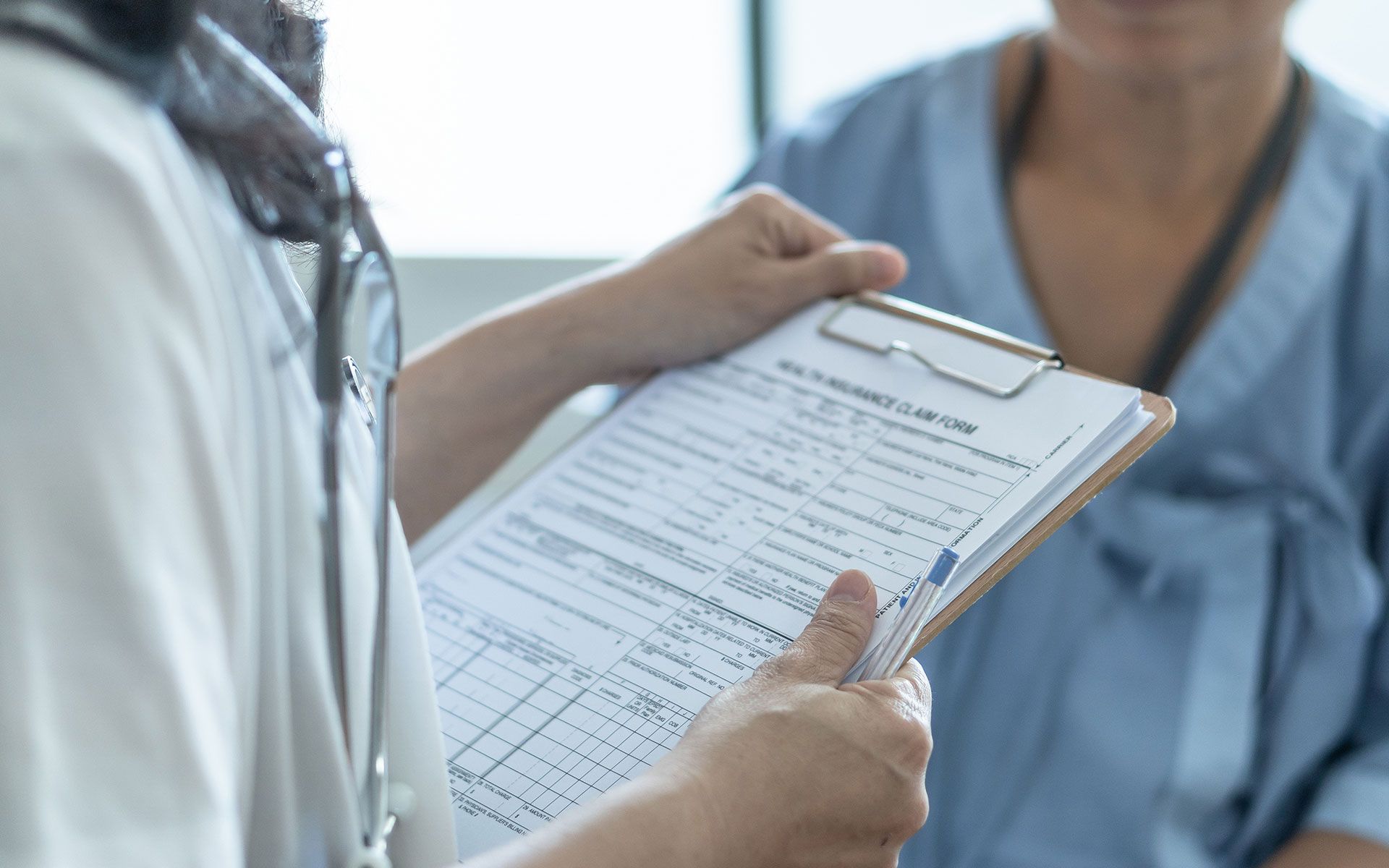Doctor holding clipboard, interviewing patient in a blue gown.