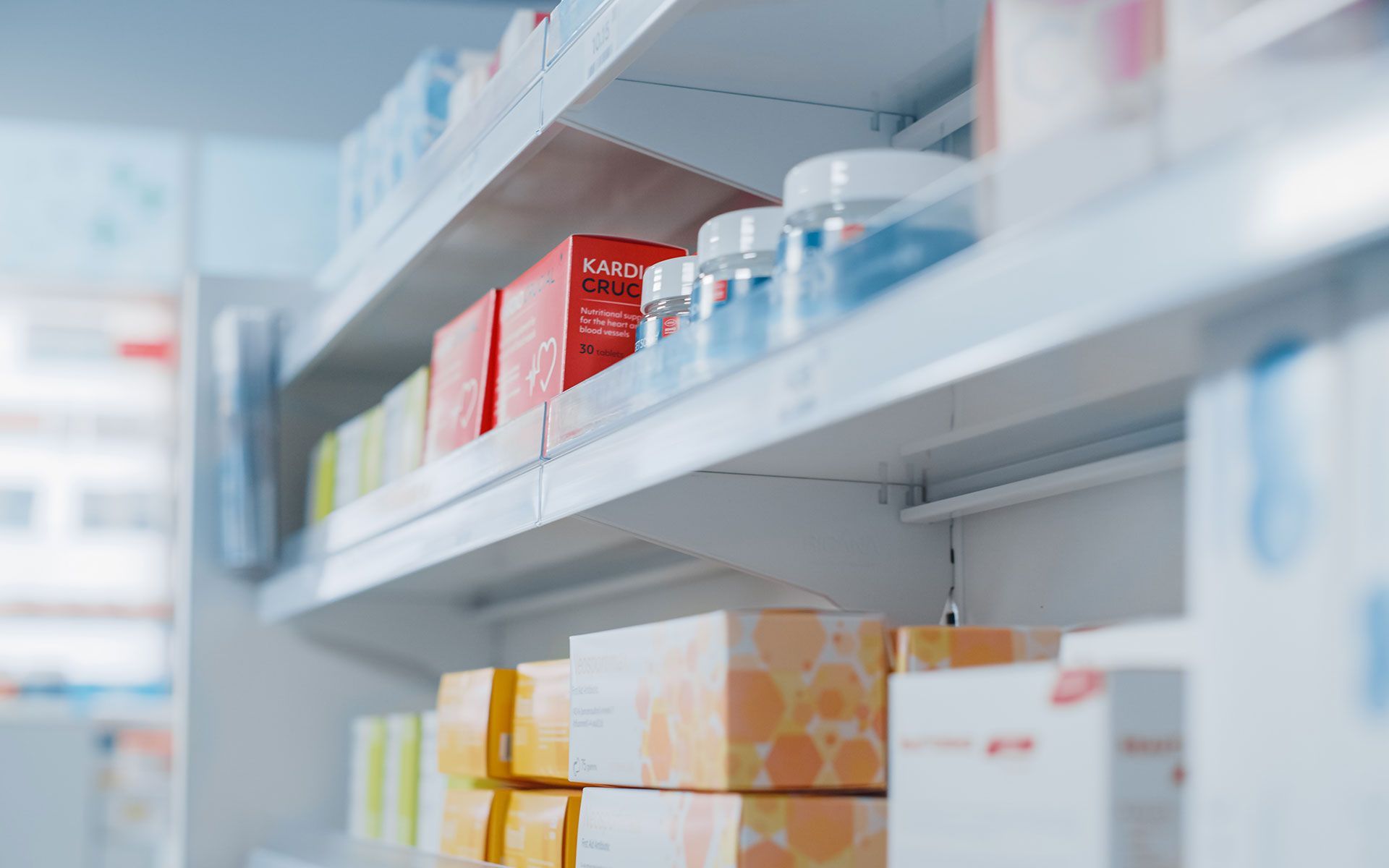 Shelves in a pharmacy filled with various medications in boxes and jars, primarily white, red, yellow, and blue.