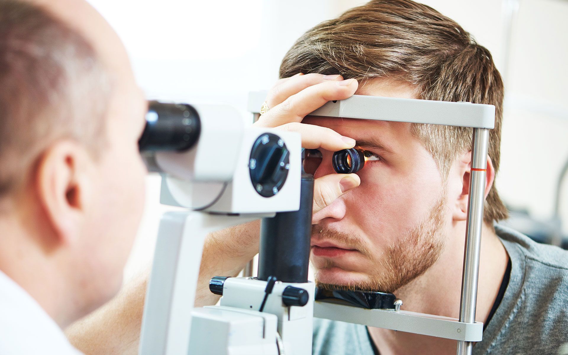Man receiving an eye exam with a slit lamp by an optometrist in an exam room.