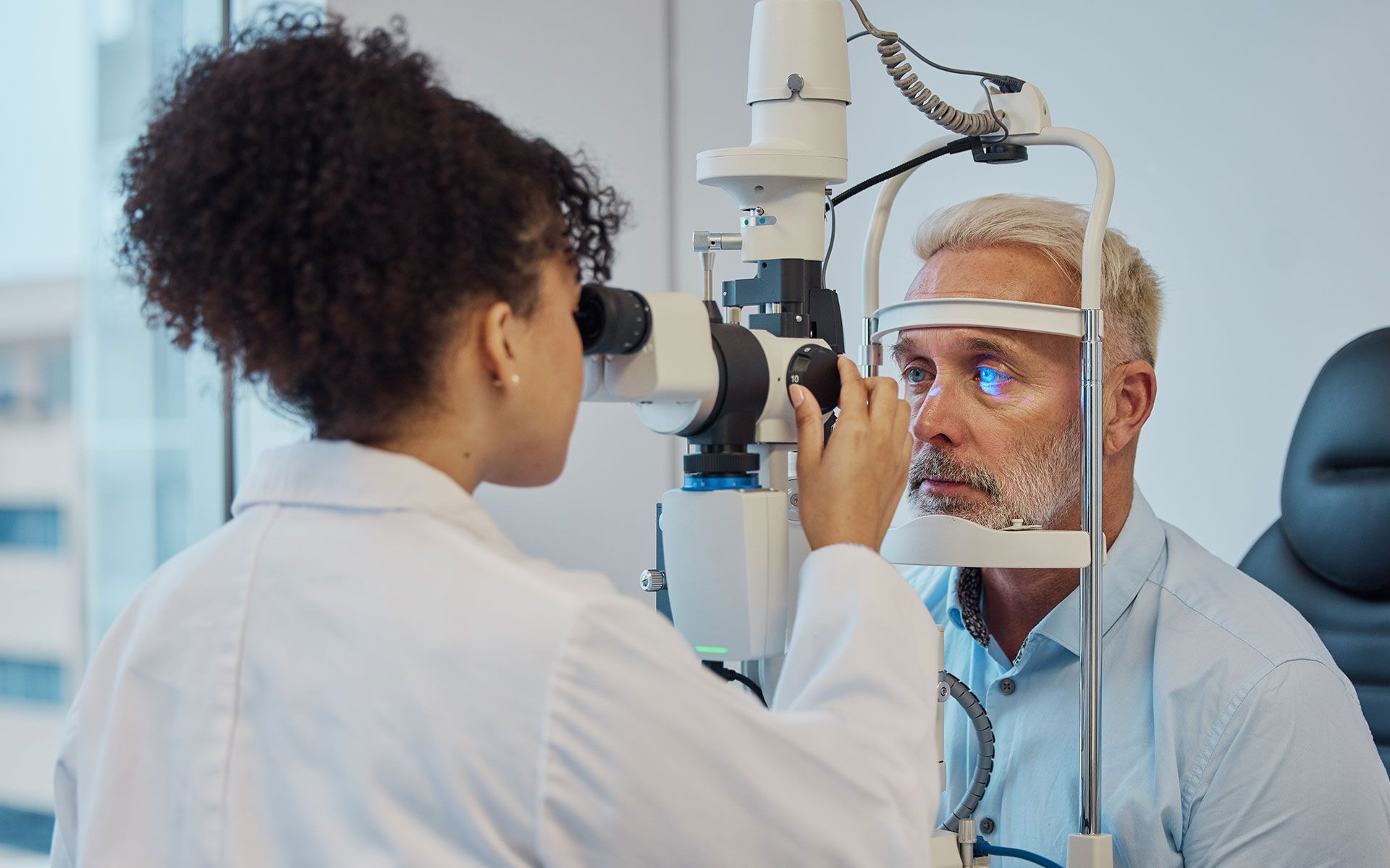 Optometrist examining a man's eye with a slit lamp in a clinic setting.