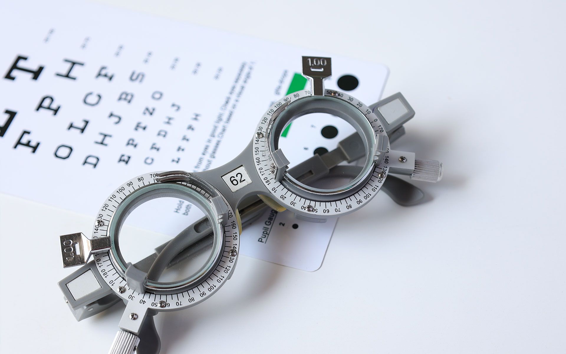 Trial frame glasses and eye chart on a white surface, used for an eye exam.