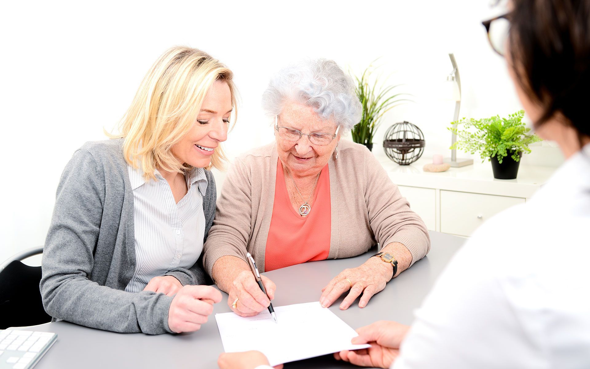 Woman and daughter signing a document with assistance from a medical professional in an office setting.