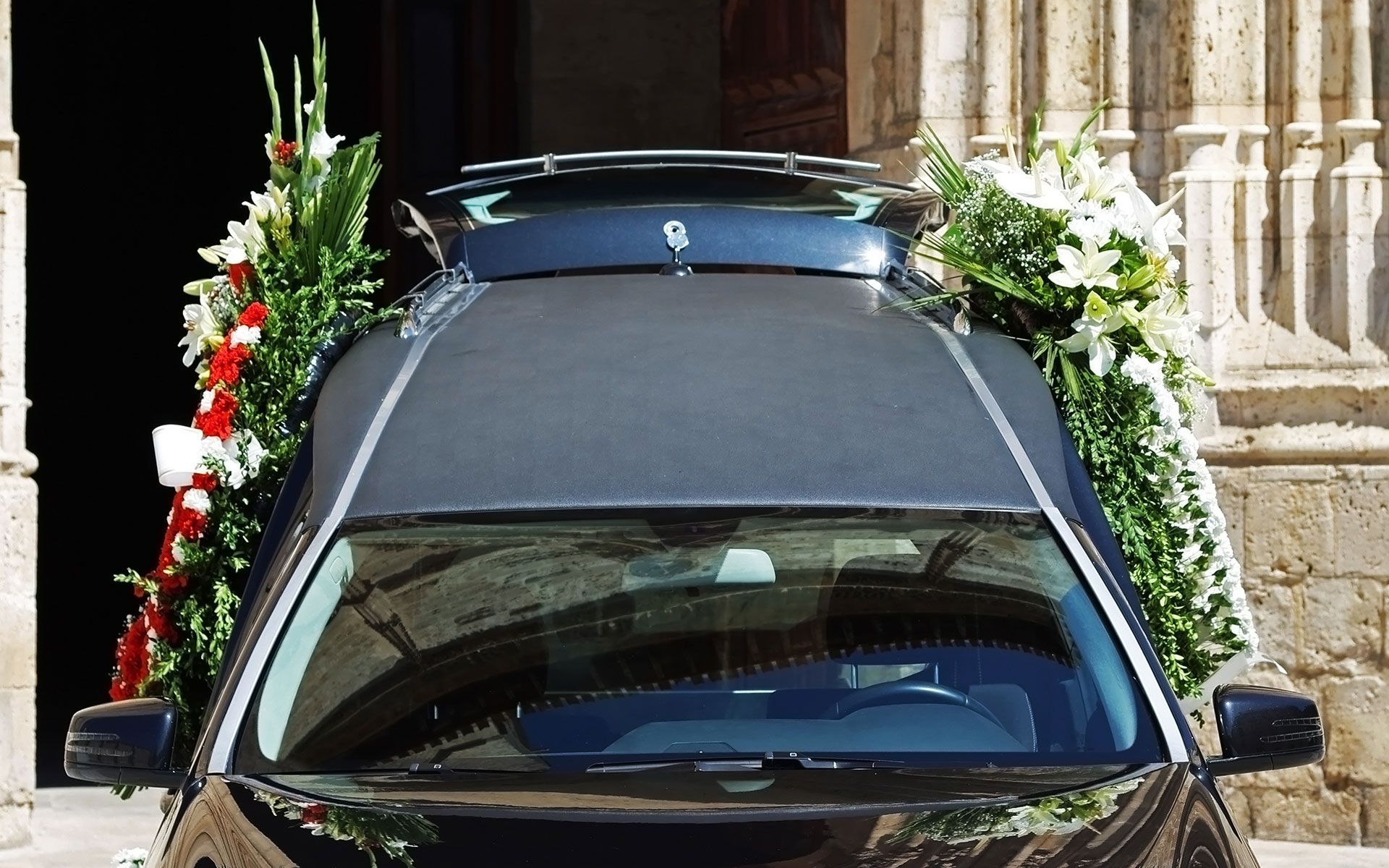 Black hearse with floral arrangements at a church entrance.