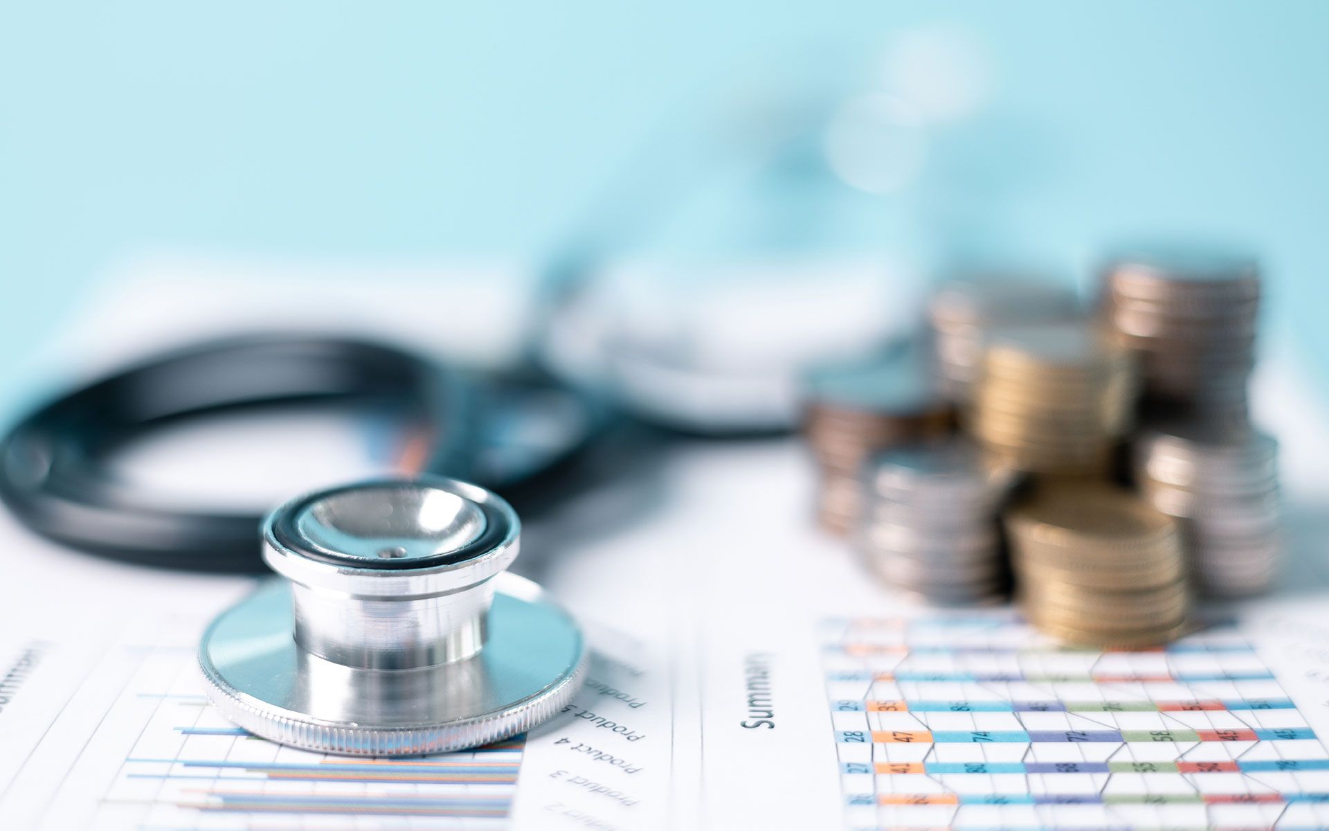 Stethoscope on financial documents with stacks of coins, representing healthcare costs and financial analysis.