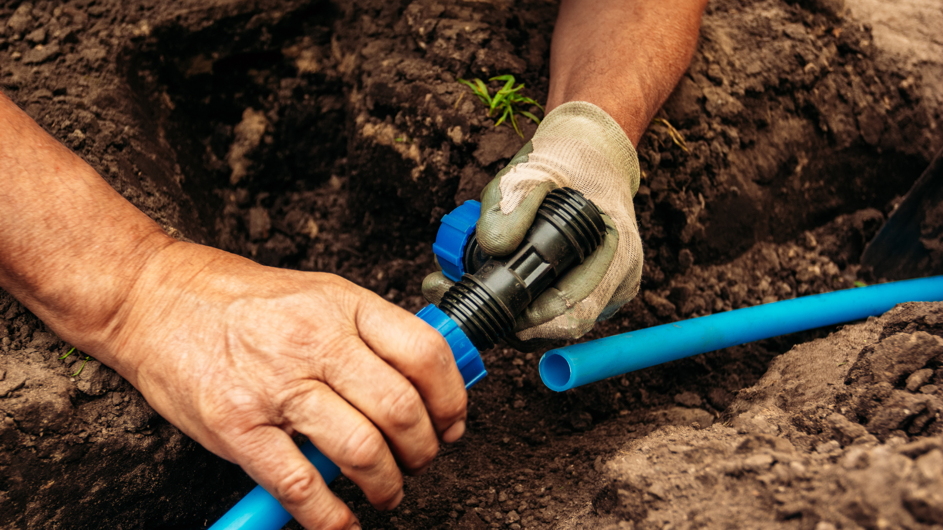 A man is fixing a hose in the dirt.