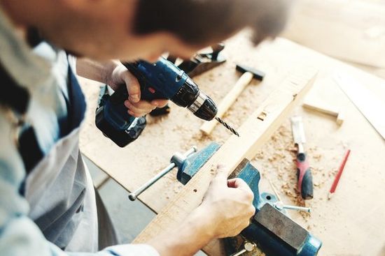 Picture of a man using an electric drill on a board.